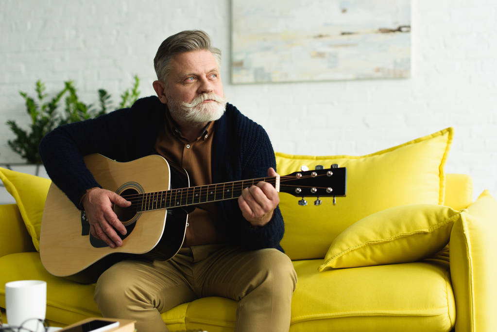 homem idoso barbudo pensivo tocando guitarra e olhando para casa
 - Foto, Imagem