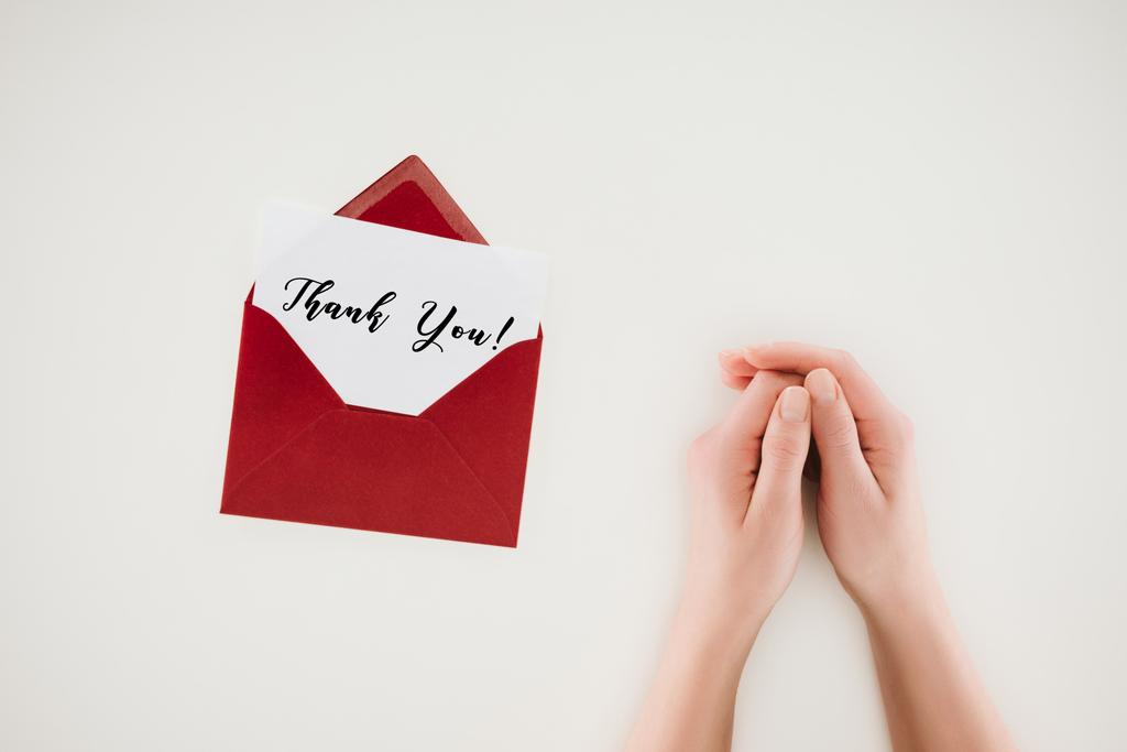 abgeschnittene Aufnahme einer Frau beim Händchenhalten in der Nähe eines geöffneten roten Umschlags mit Dankeschön-Schriftzug auf weißem Papier - Foto, Bild