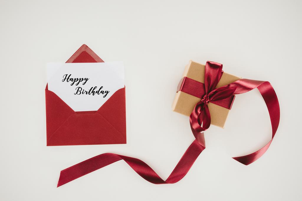 Ansicht von oben roter Umschlag mit Happy Birthday Schriftzug auf Papier und Geschenkschachtel isoliert auf Weiß - Foto, Bild