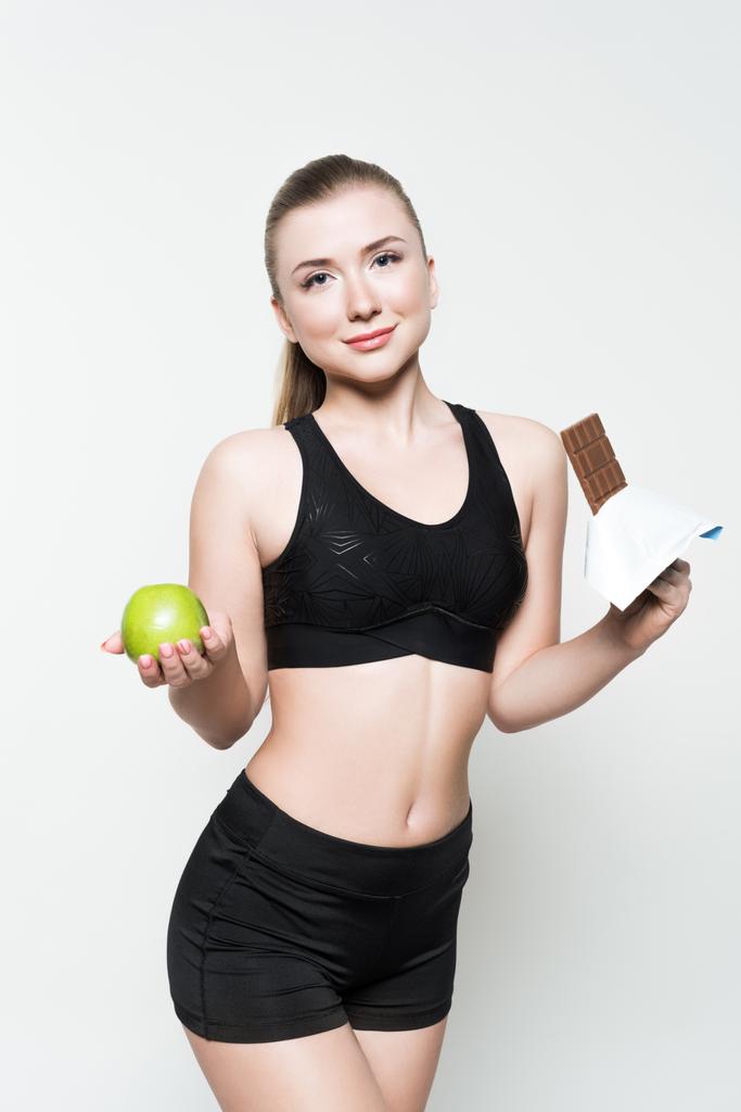 Підійде дівчина тримає яблуко і шоколадний батончик ізольовано на білому
 - Фото, зображення