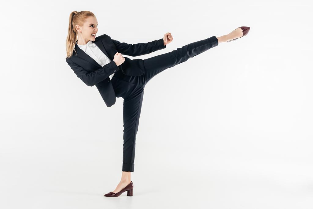 zakenvrouw uitvoeren van karate kick in pak en hoge hakken op wit wordt geïsoleerd - Foto, afbeelding