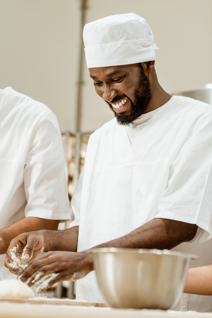 handsome african american baker kneading dough for pastry at baking manufacture - Photo, Image