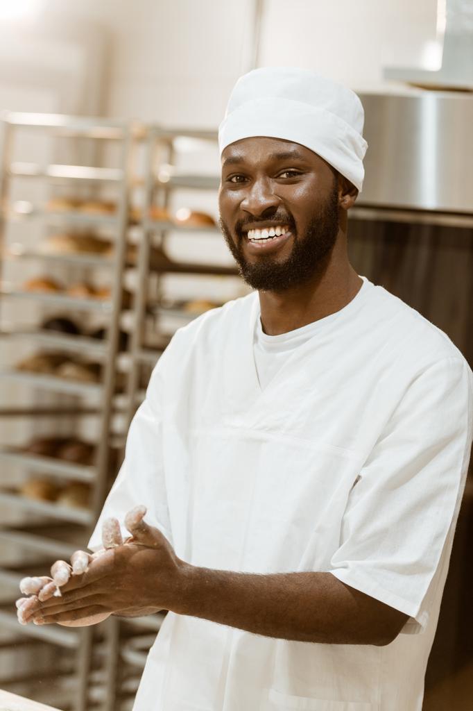 handsome african american baker with flour on hands at baking manufacture - Photo, Image