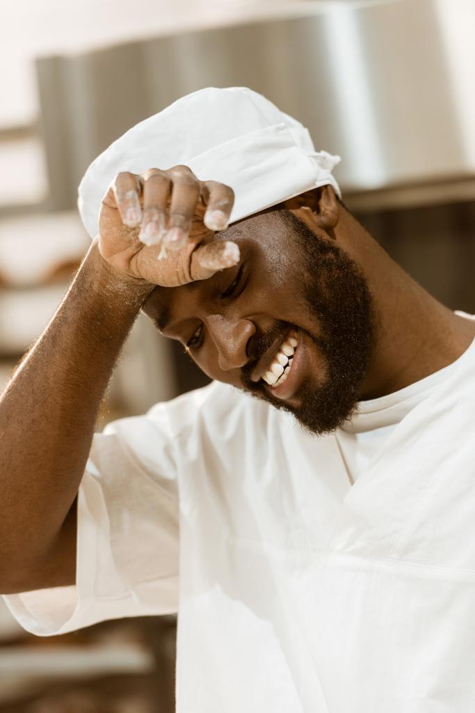 tired african american baker wiping sweat on baking manufacture - Photo, Image