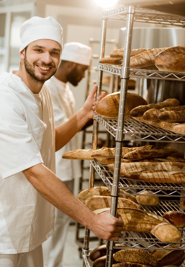 пекарь возле полок со свежими хлебами при выпечке
 - Фото, изображение