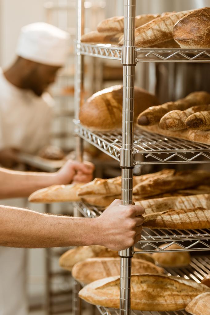 tiro recortado de panadero que sostiene estantes con panes frescos en la fabricación de la hornada
 - Foto, Imagen