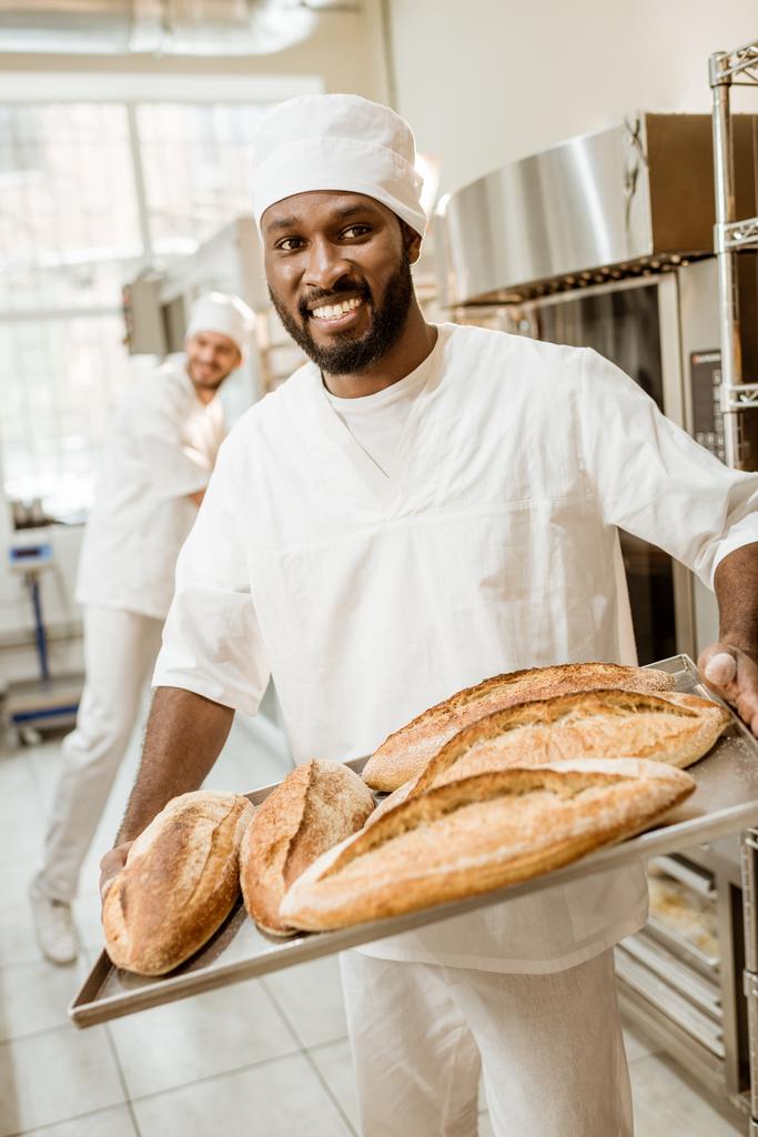 Afrikanisch-amerikanischer Bäcker holt bei Backmanufaktur Brotlaibe aus dem Ofen - Foto, Bild