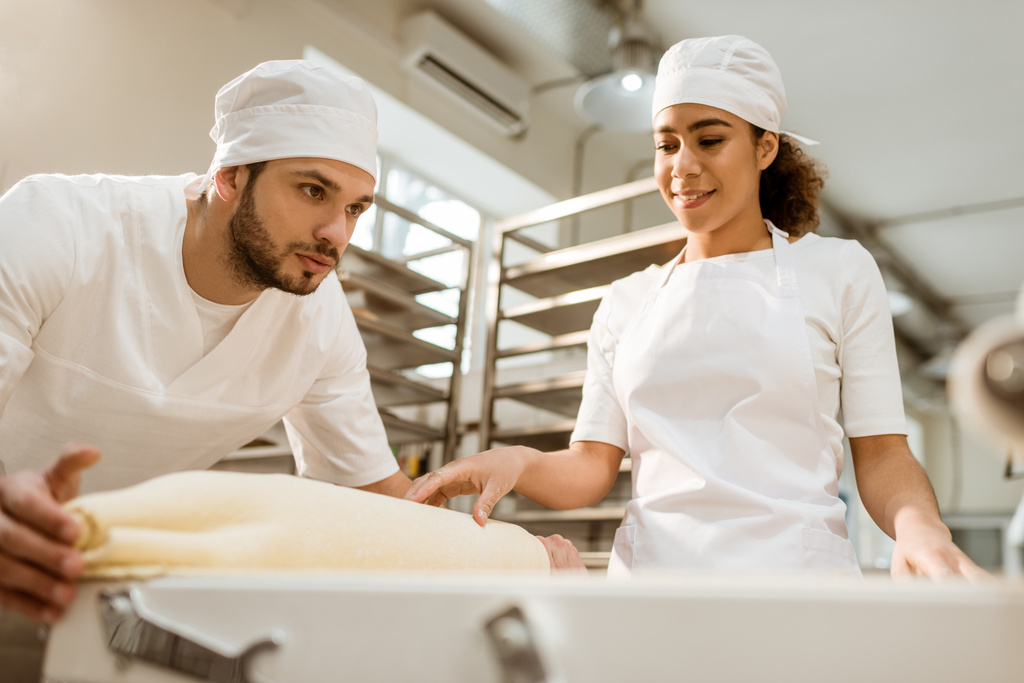 nuoret leipurit, jotka työskentelevät teollisen taikinarullan kanssa leivonnan valmistuksessa
 - Valokuva, kuva