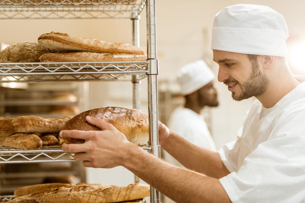 komea hymyilevä leipuri laittaa tuoretta leipää hyllylle leivontaan valmistus
 - Valokuva, kuva