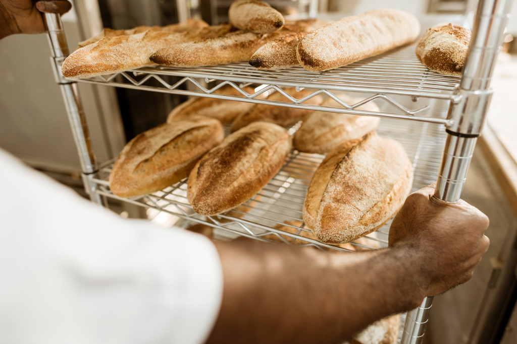 tiro recortado de panadero que conduce estantes de pan fresco en la fabricación de la hornada
 - Foto, imagen