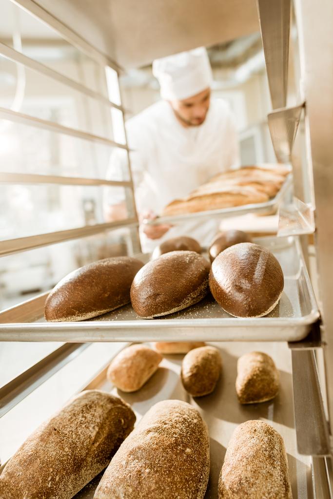 padeiro colocando bandejas de pão fresco em stand na fabricação de cozimento
 - Foto, Imagem