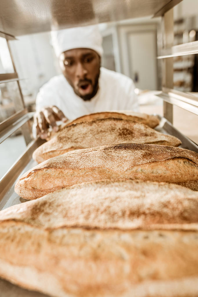 podekscytowany african american baker patrząc świeże bochenków chleba na pieczenia produkcji - Zdjęcie, obraz