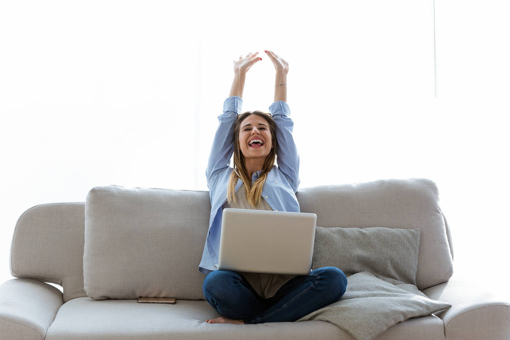 schöne junge Frau feiert einen Erfolg, während sie zu Hause mit Laptop arbeitet. - Foto, Bild