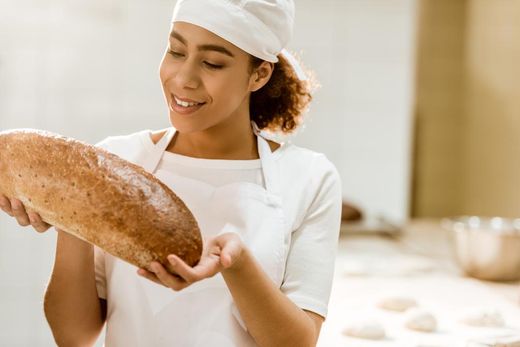 Bayan baker taze somun ekmek üretimi pişirme üzerinde tutan gülümseyerek - Fotoğraf, Görsel