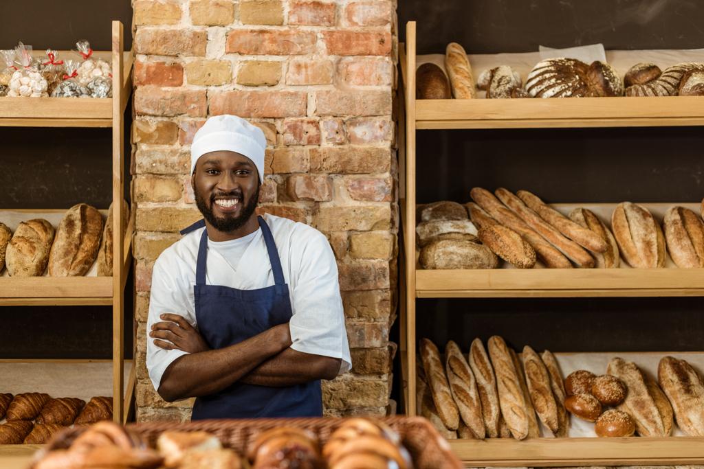 guapo panadero sonriente con los brazos cruzados de pie en la pastelería
 - Foto, imagen