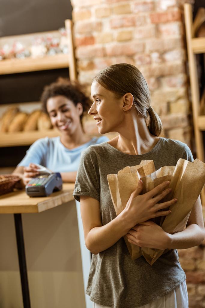 onnellinen nuori nainen lähtee leivonnaiset myymälä eri leipää paperipusseissa
 - Valokuva, kuva