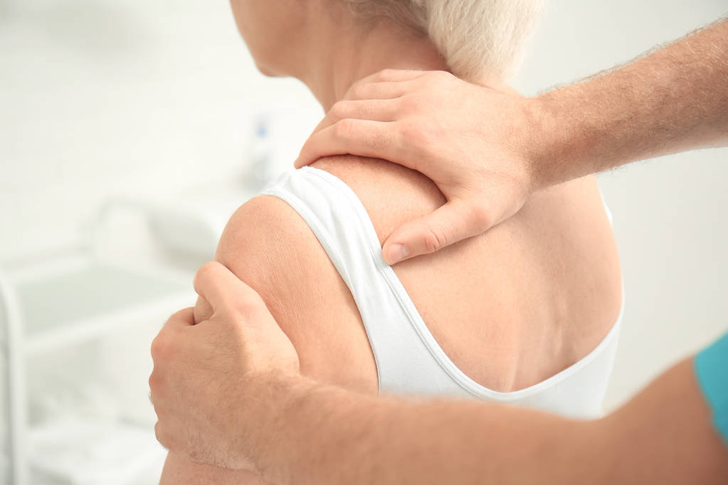 Bejaarde vrouw krijgen schouder massage bij fysiotherapie kantoor - Foto, afbeelding