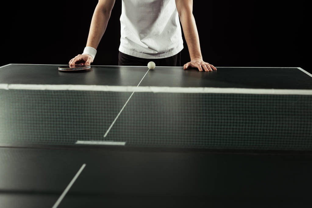 cropped shot of tennis player leaning on tennis table with racket and ball isolated on black - Photo, Image