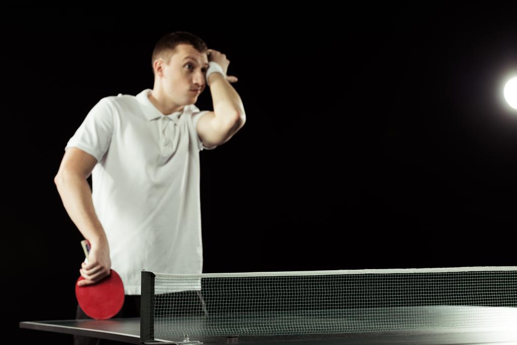 Müder Tennisspieler in Uniform neben Tischtennisplatte isoliert auf Schwarz - Foto, Bild