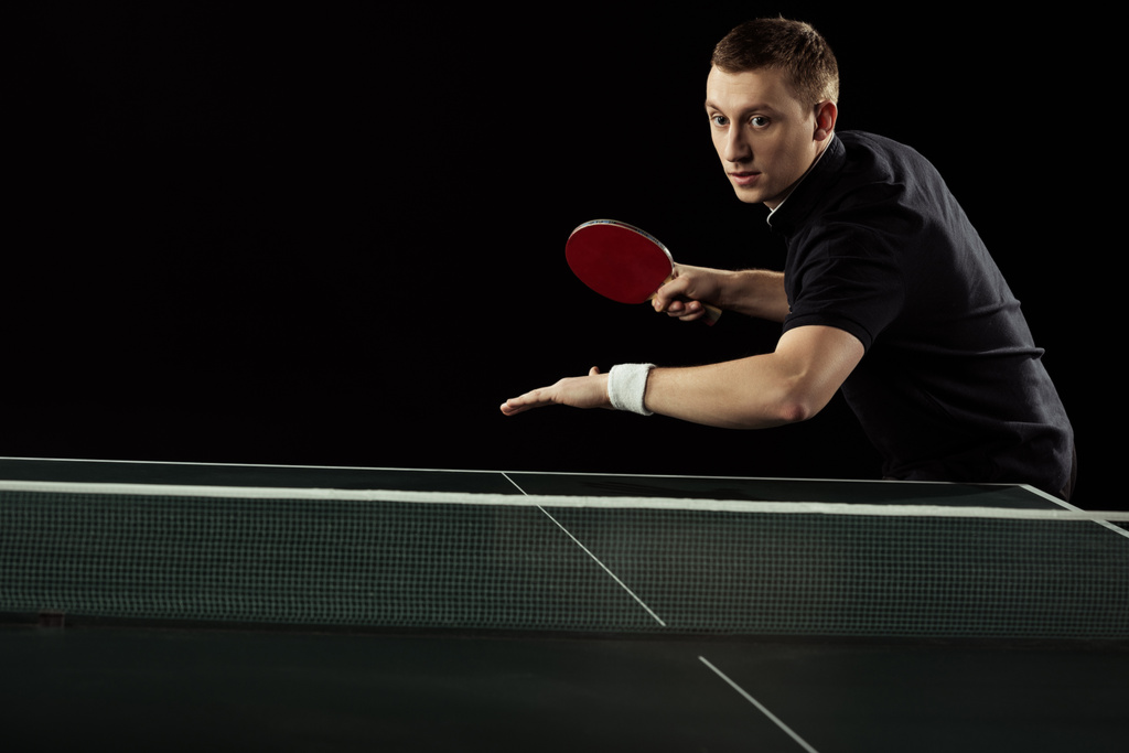 πορτρέτο του εστιασμένη τένις παίκτης παίζει πινγκ πονγκ που απομονώνονται σε μαύρο - Φωτογραφία, εικόνα