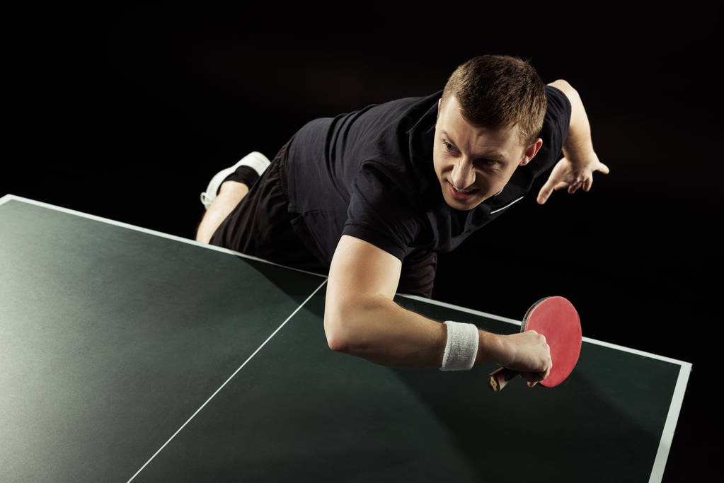 joueur de tennis émotionnel en uniforme jouant au tennis de table isolé sur noir
 - Photo, image
