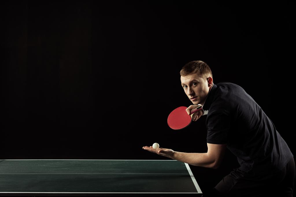 Zijaanzicht van jonge tafeltennisser met racket en bal in handen geïsoleerd op zwart - Foto, afbeelding