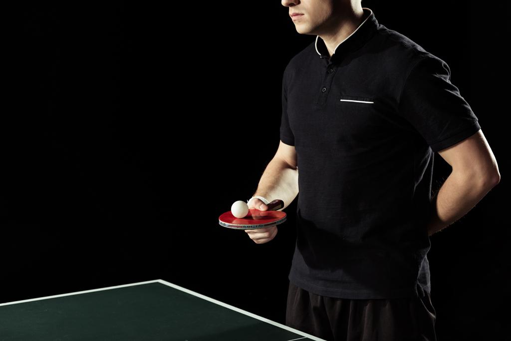 gedeeltelijke weergave van tennisser tennisbal op racket in de hand houden geïsoleerd op zwart - Foto, afbeelding
