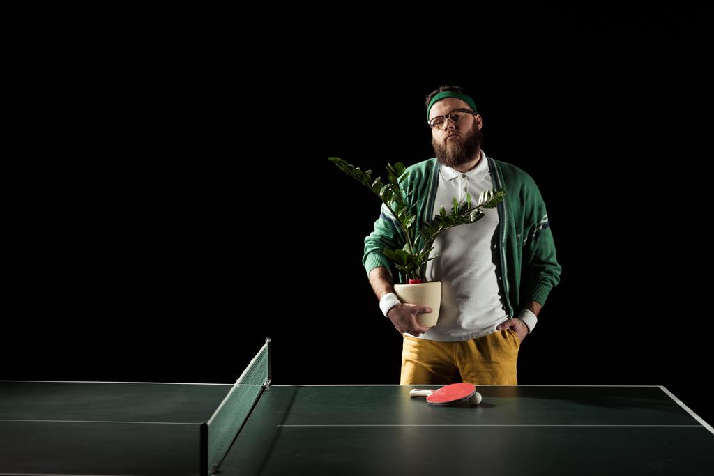 bearded man with flower in pot standing at tennis table isolated on black - Photo, Image