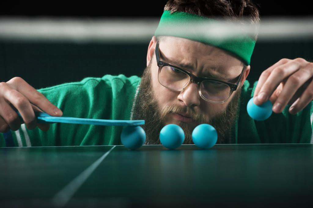 bearded tennis player looking at blue tennis balls on table isolated on black - Photo, Image