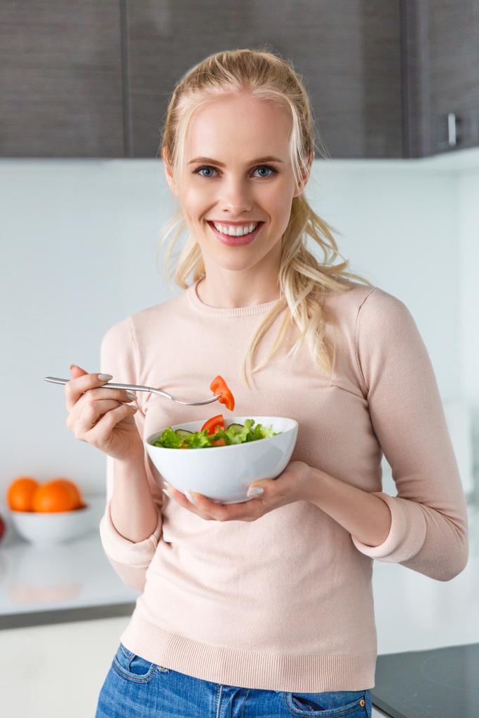 hermosa mujer joven comiendo ensalada de verduras frescas y sonriendo a la cámara
 - Foto, Imagen