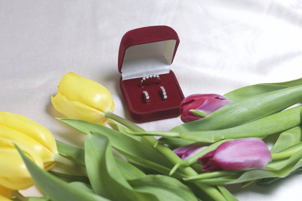 Presentes para entes queridos. Um buquê de tulipas amarelas e rosa é espalhado em uma superfície leve. Nas proximidades é uma caixa de veludo aberta de cor vermelha com jóias de ouro
. - Foto, Imagem