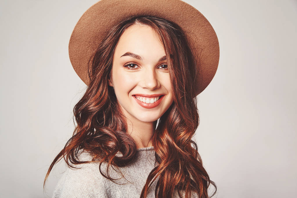 Portret młodego stylowe roześmiany dziewczyna model w szare codzienne letnie ubrania w brązowy kapelusz z naturalny makijaż na białym tle na szarym tle. Patrząc na kamery - Zdjęcie, obraz