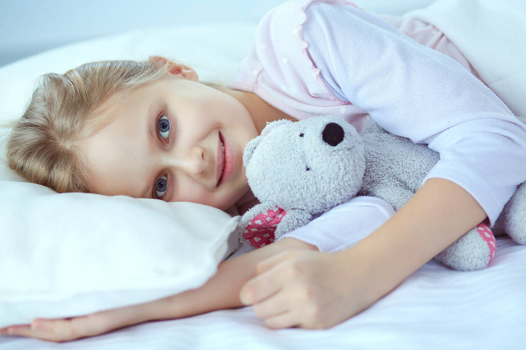 kind meisje slaapt in het bed met een speeltje teddy beer - Foto, afbeelding