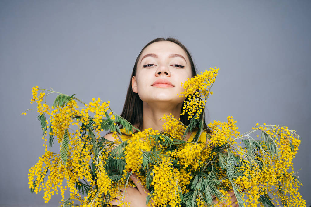 Młoda kobieta z bukietem żółte kwiaty w ręce na szarym tle - Zdjęcie, obraz