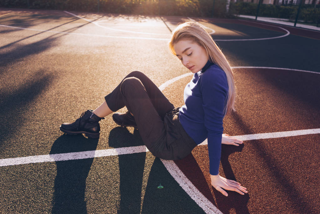 girl in blue sweater sits on sports field in sun - Photo, Image