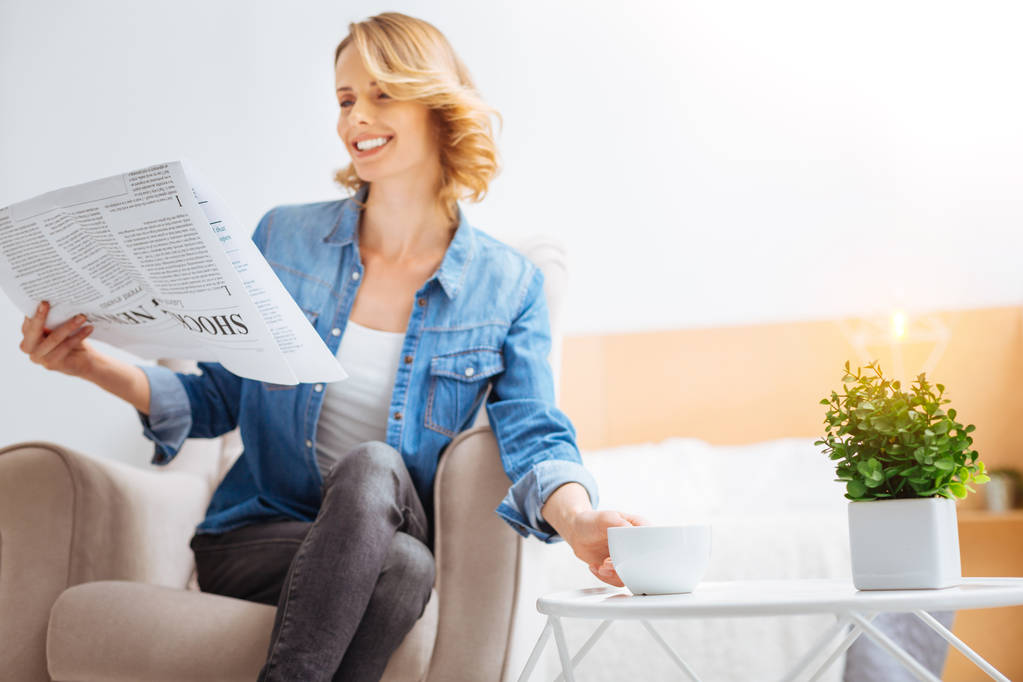 Happy cheerful woman reading her favorite newspaper and smiling - Photo, Image