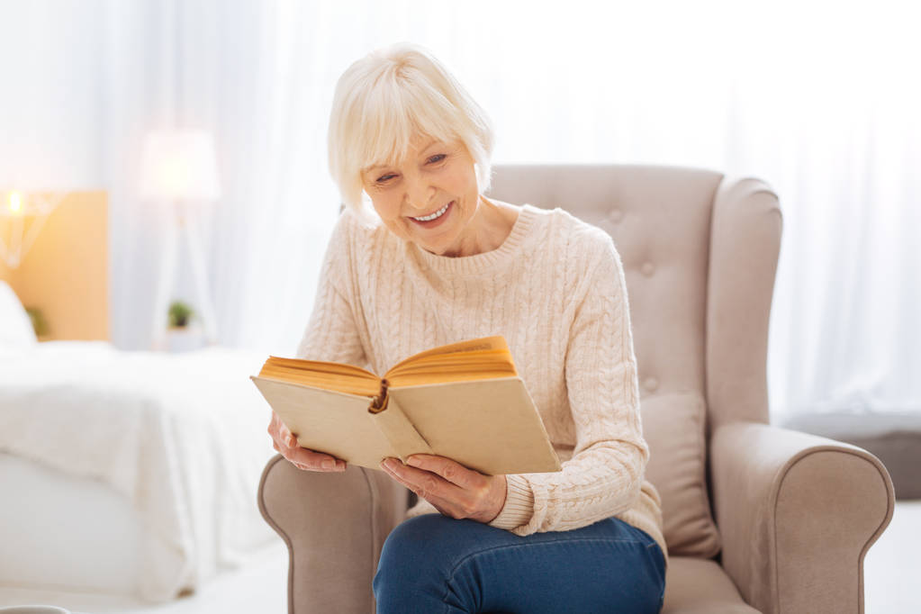Happy aged woman feeling good while reading an interesting book - Photo, Image