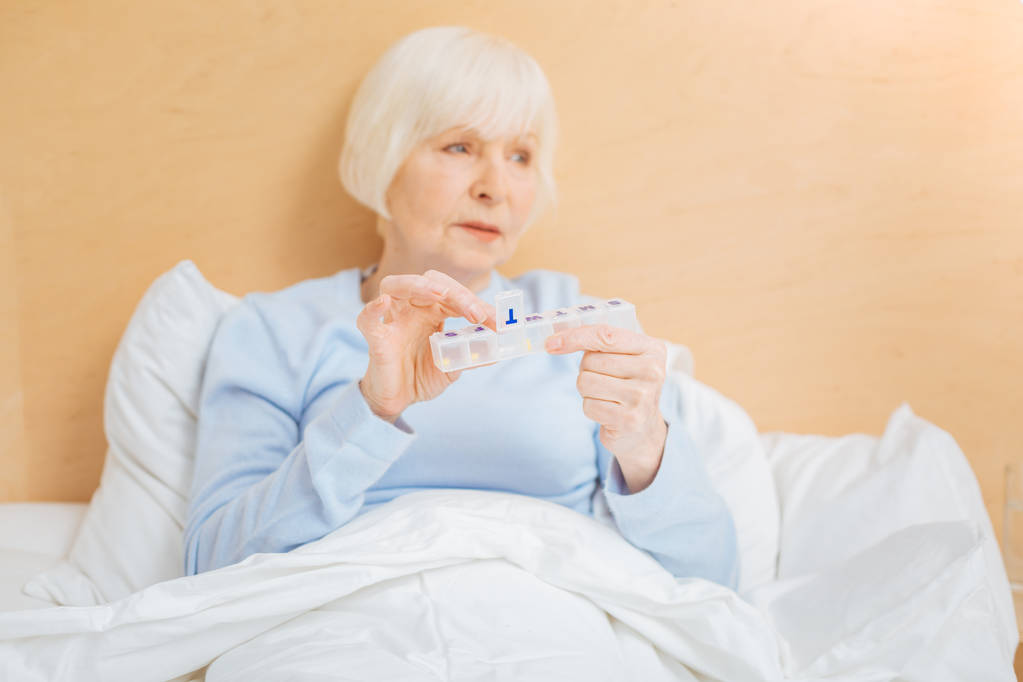 Zieke ouder vrouw zit met haar pillendoos en kijken in de verte - Foto, afbeelding