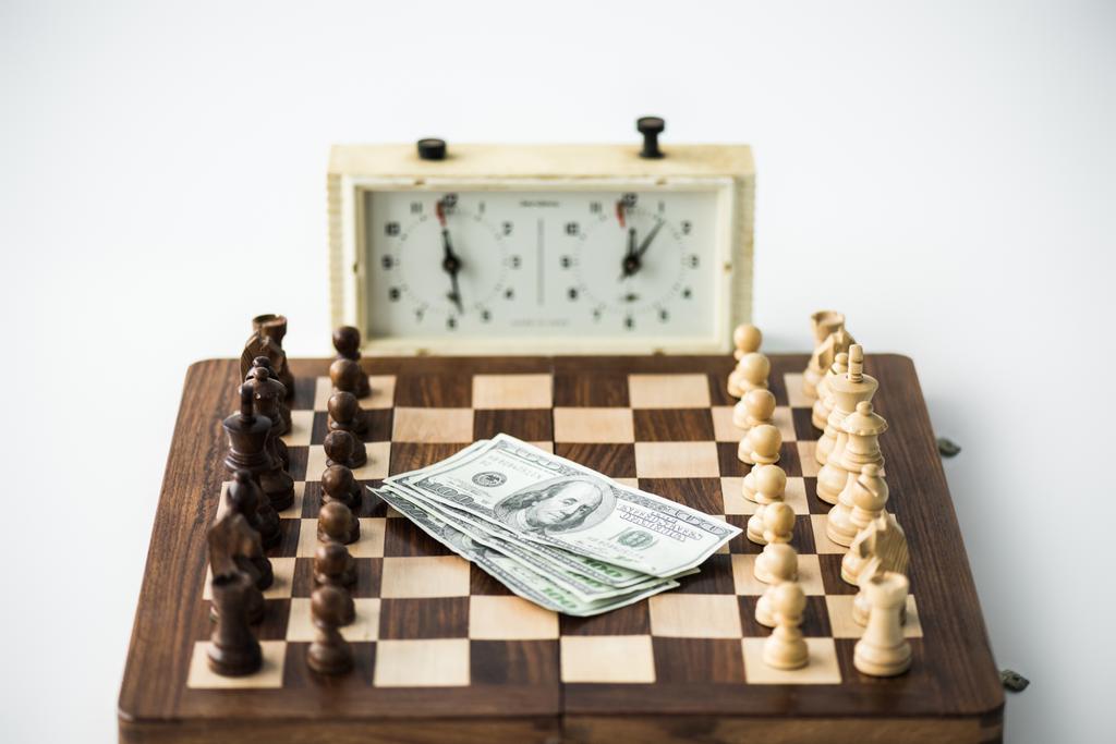 Relógio de xadrez perto do tabuleiro de xadrez com figuras e notas de dólar isoladas em branco
 - Foto, Imagem