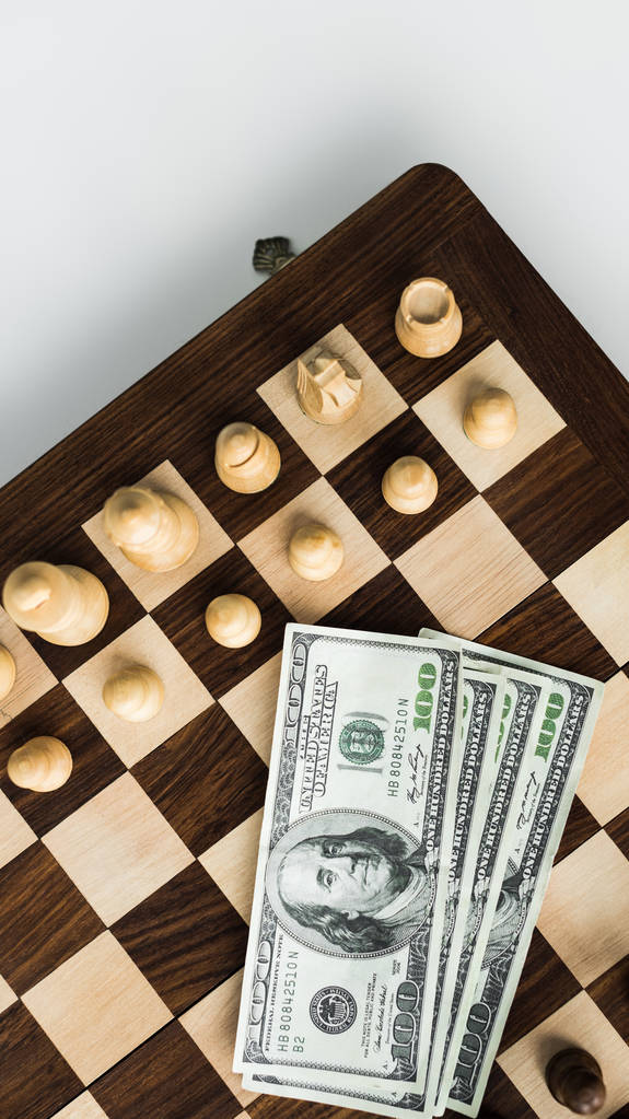Vue du dessus de l'échiquier avec billets en dollars et pièces d'échecs sur la surface blanche
 - Photo, image