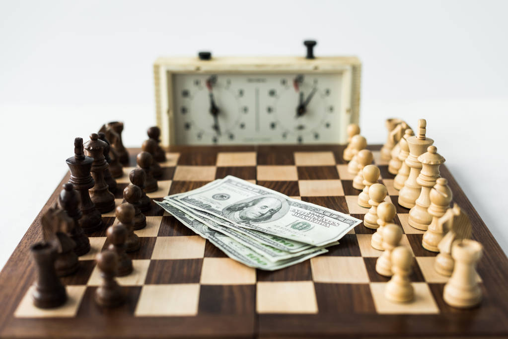 Шахматная доска с деньгами и фигурами возле шахматных часов изолирована на белом
 - Фото, изображение