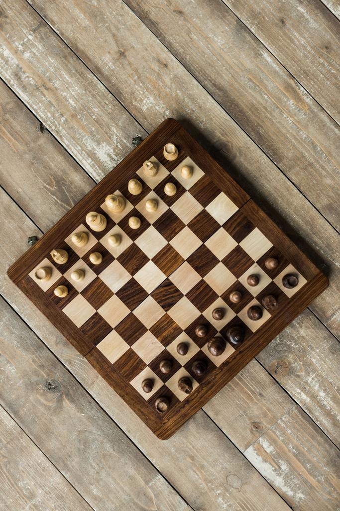 Вид сверху шахматной доски с шахматными фигурами, установленными для новой игры на деревянной поверхности
 - Фото, изображение