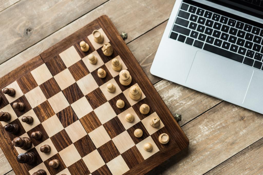 Laptop i szachy deska z postaciami na rustykalne drewniane powierzchni - Zdjęcie, obraz
