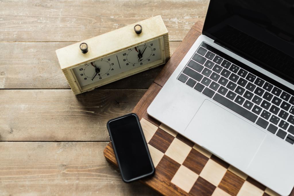 Orologio a scacchi, smartphone, laptop e scacchiera su superficie in legno
 - Foto, immagini