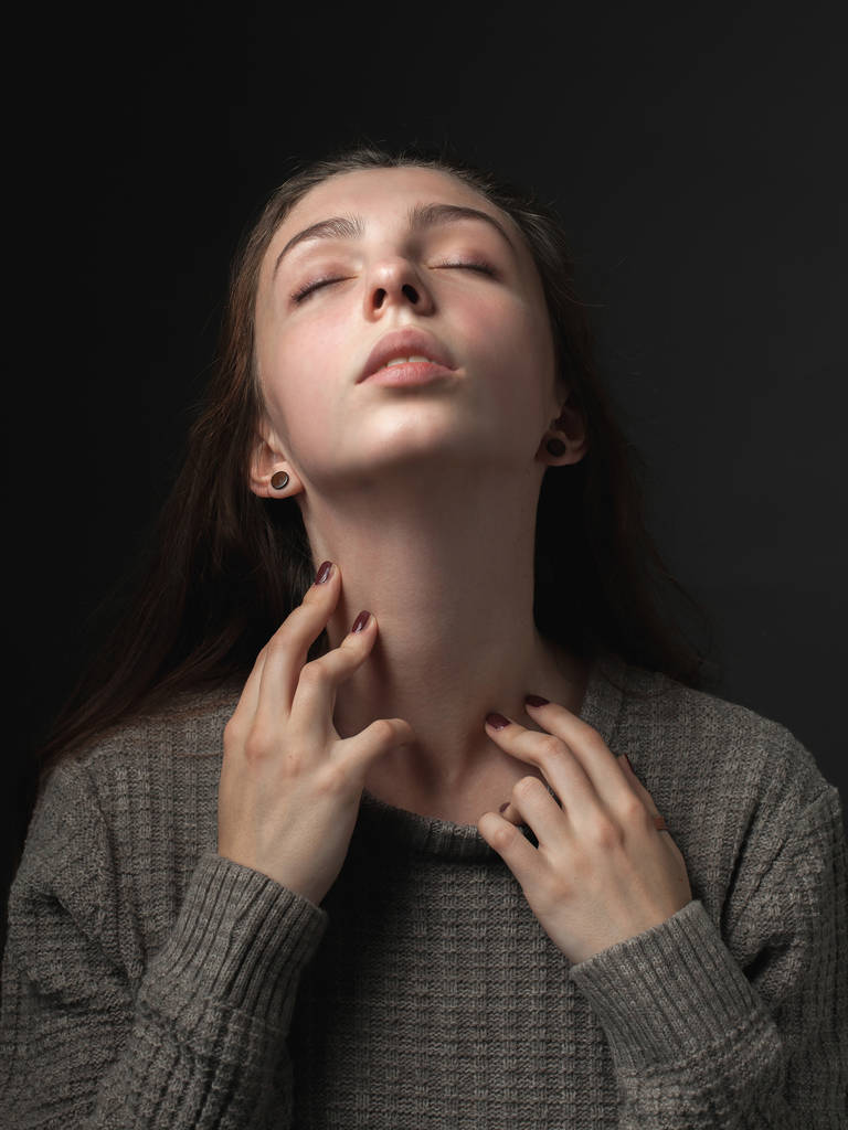 Retrato de mujer joven con las manos tocando el cuello sobre fondo gris
 - Foto, Imagen
