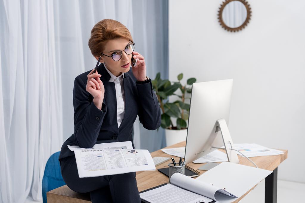 mujer de negocios con documentos hablando en el teléfono inteligente en el lugar de trabajo en la oficina
  - Foto, imagen