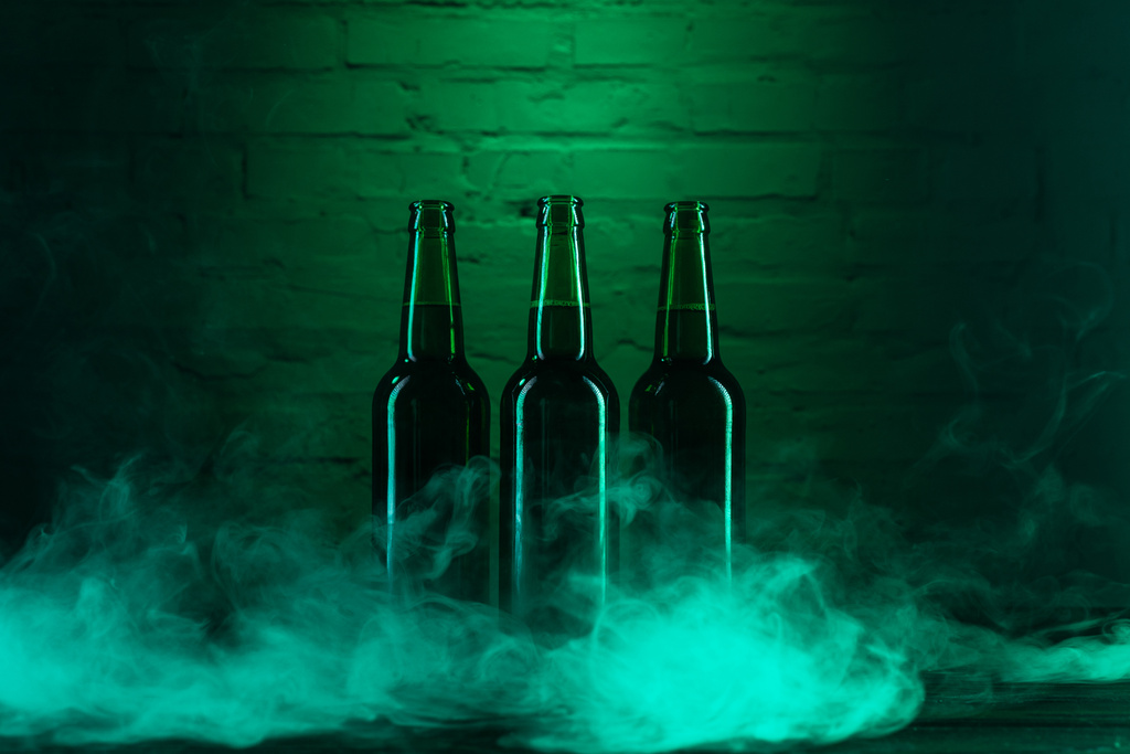 3 つの緑色のビール瓶と緑のれんが造りの壁の近くの煙 - 写真・画像
