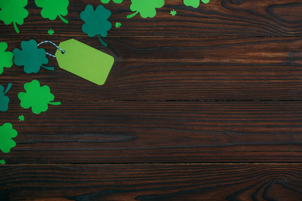 Draufsicht auf leeres grünes Etikett und Shamrocks auf Holztisch - Foto, Bild