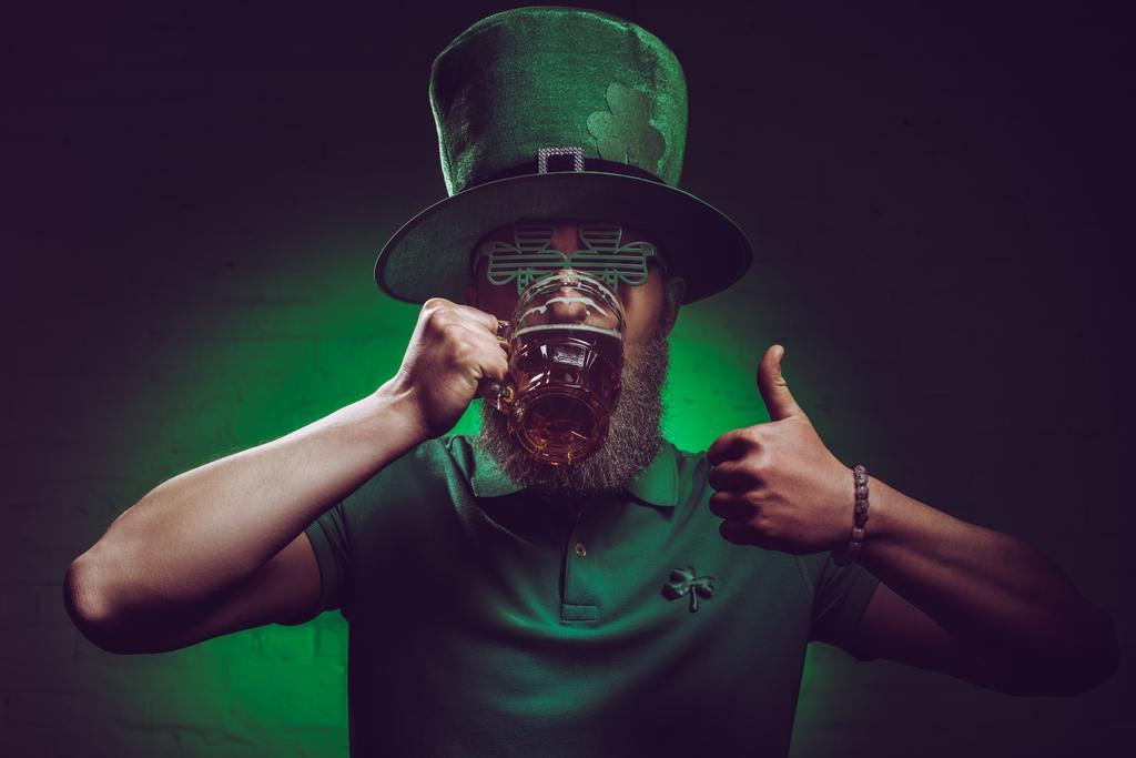 barbudo homem em verde irlandês chapéu beber cerveja e mostrando polegar para cima
 - Foto, Imagem