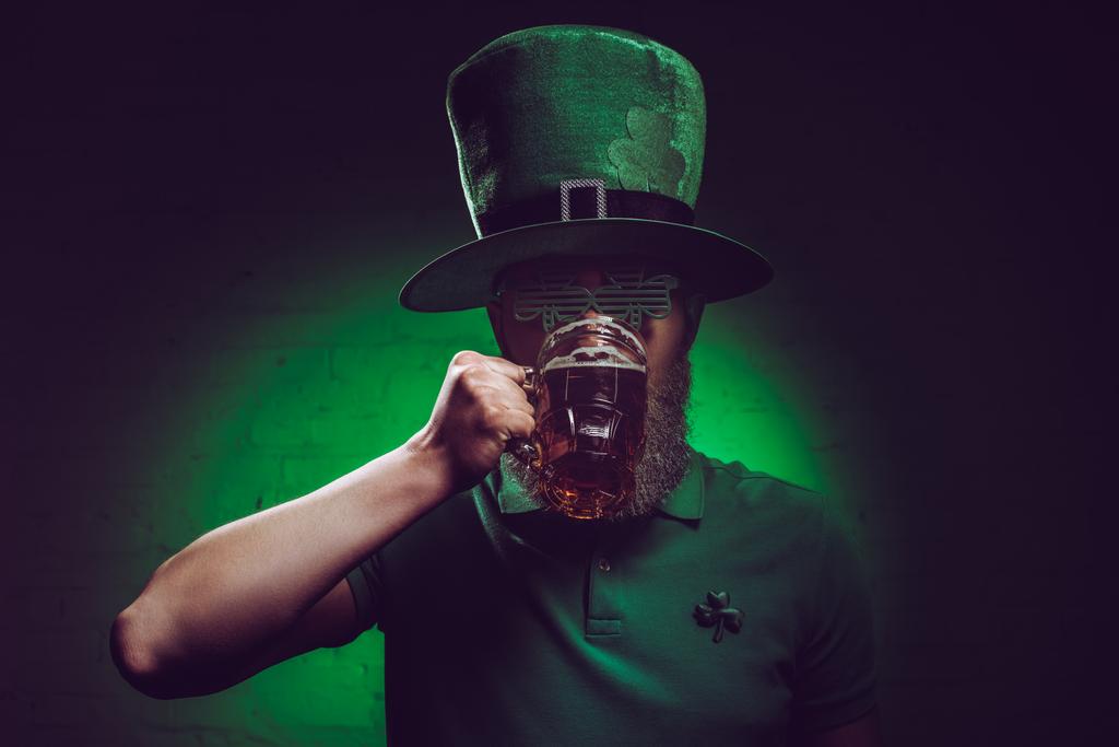 jonge bebaarde man in groen Ierse hoed bier drinken - Foto, afbeelding